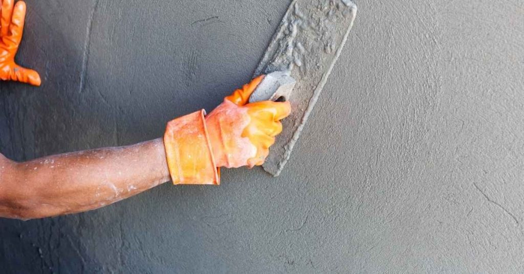 Hand wearing orange gloves smoothing gray stucco with trowel