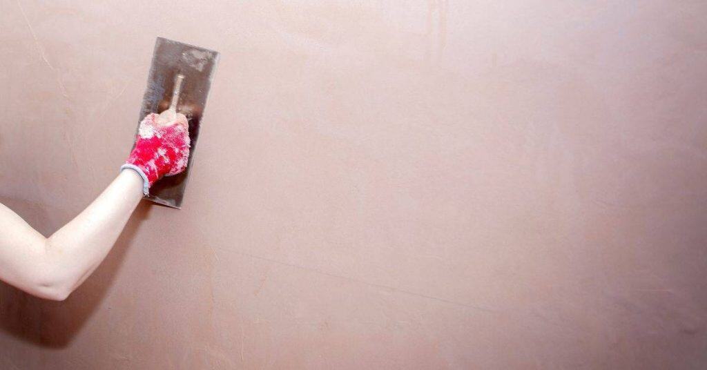 Hand wearing red glove smoothing plaster on wall with trowel