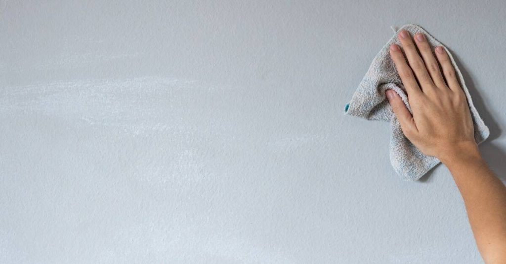 Hand wiping a smooth light gray wall with a cloth