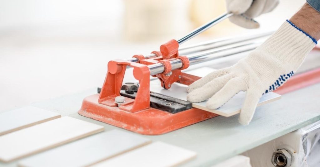 Hand with glove using manual tile cutter on tile