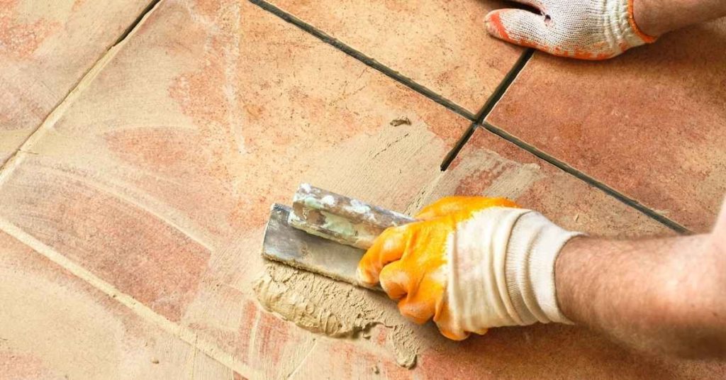 Hands applying grout between ceramic floor tiles
