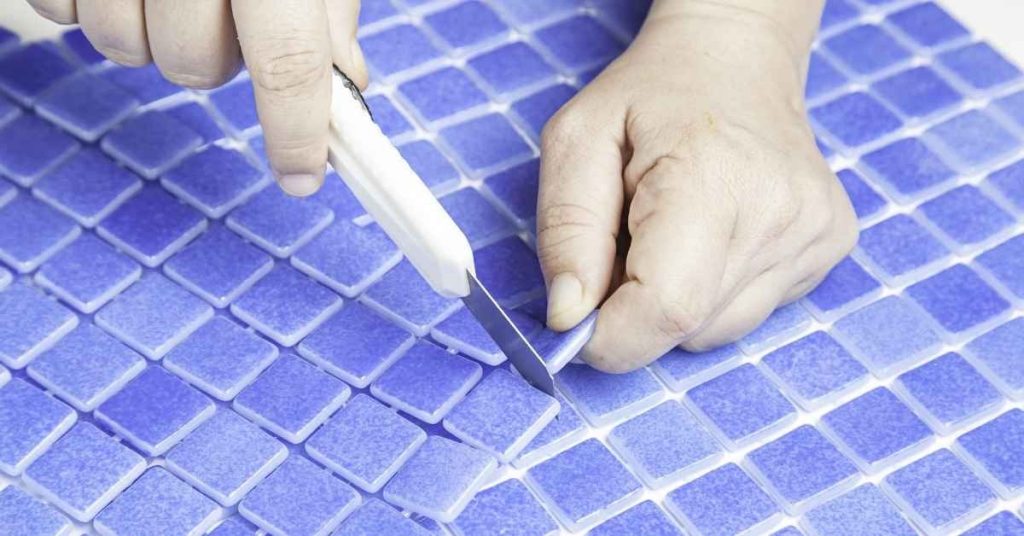 Hands cutting small blue glass mosaic tiles with a knife