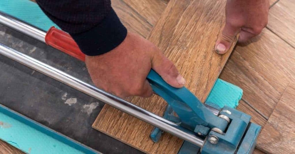 Hands cutting wood-look tile with manual tile cutter