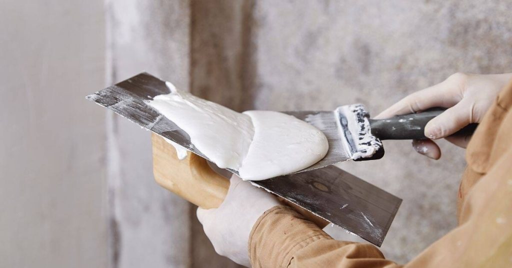 Hands holding plastering trowel and applying plaster