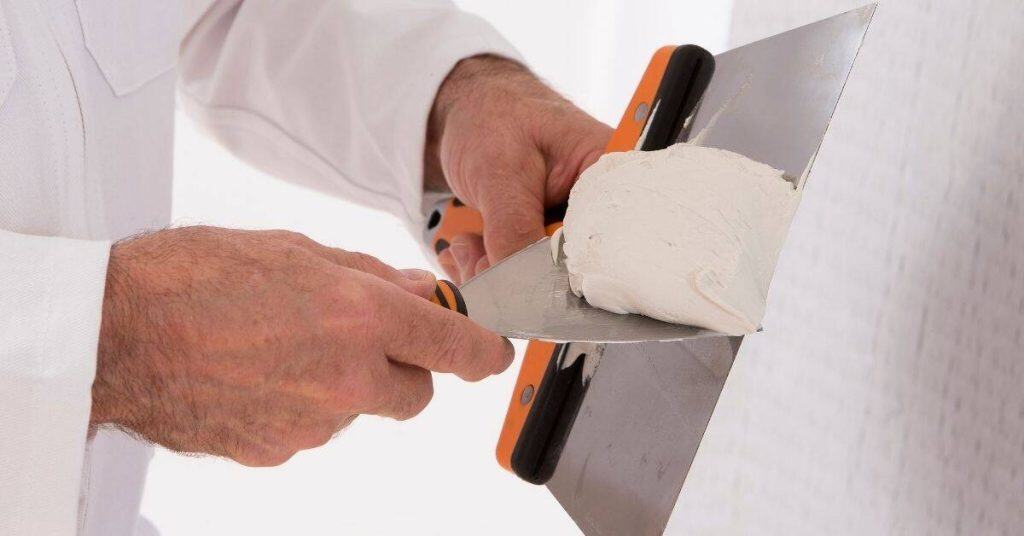 Hands holding trowel and applying white plaster