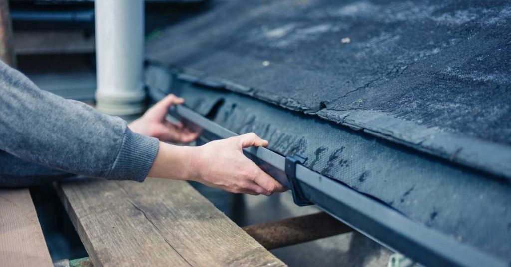 Hands installing black gutter on edge of flat roof