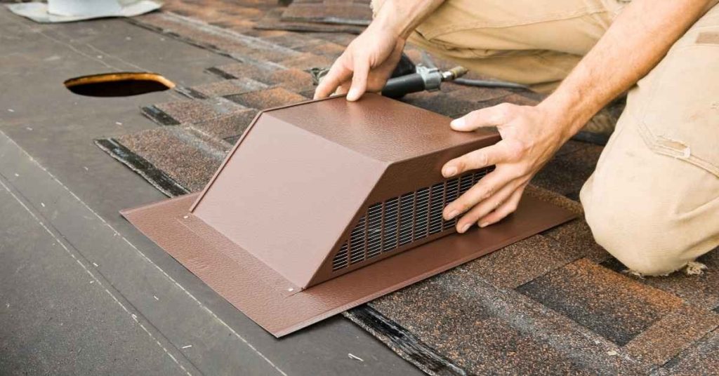 Hands installing brown roof vent flashing on shingled roof