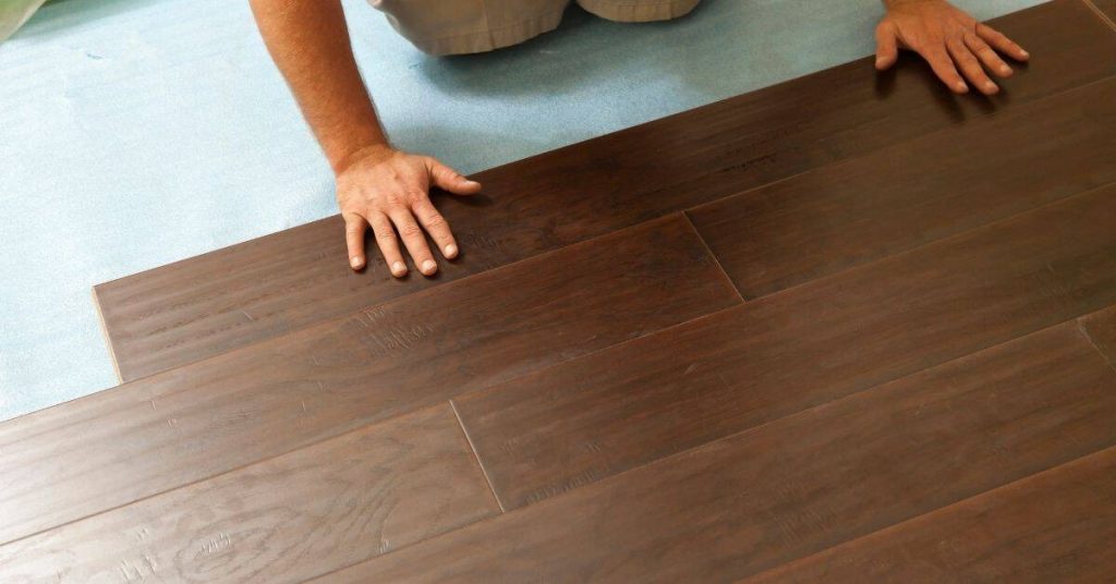 Hands installing dark brown laminate flooring planks