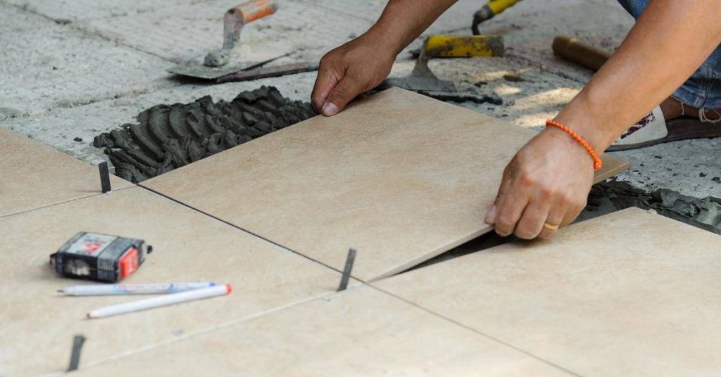 Hands placing beige floor tiles with black spacers between them