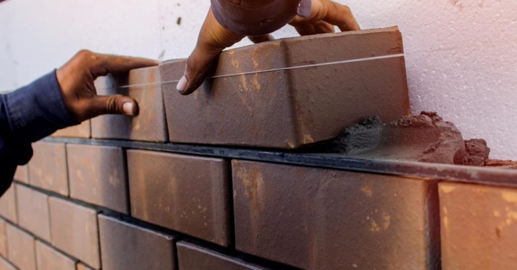 Hands placing bricks with black mortar and string line
