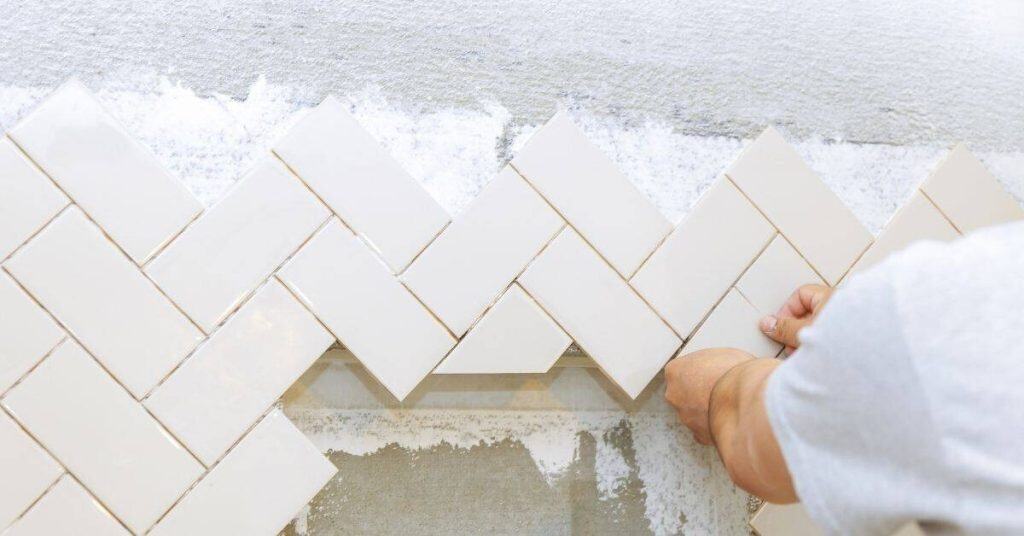 Hands placing white rectangular tiles in herringbone pattern