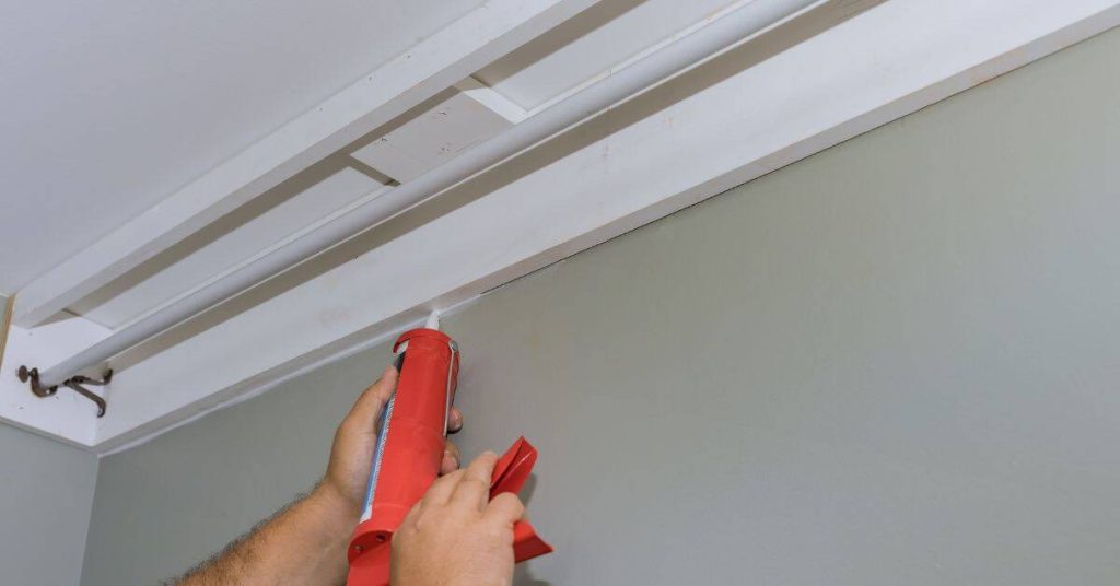 Hands tool caulk along wall and ceiling joint