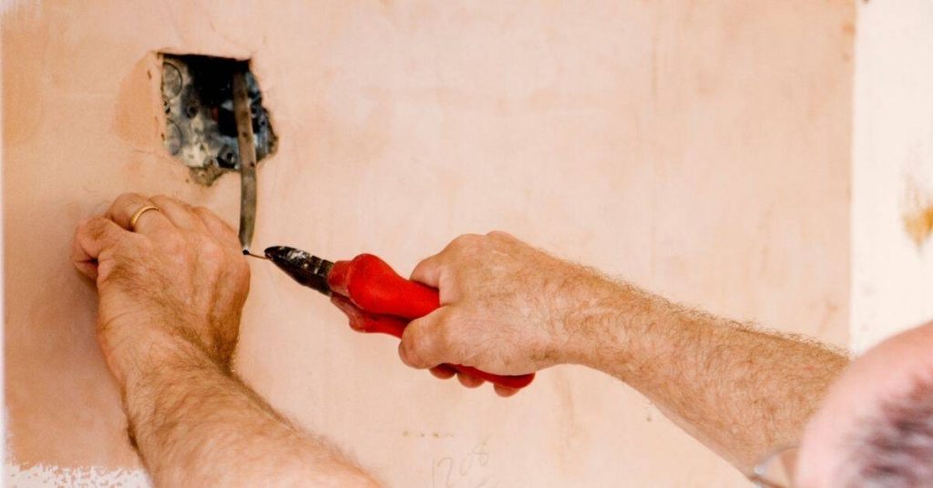 Hands using pliers to pull wire from electrical box in stucco wall