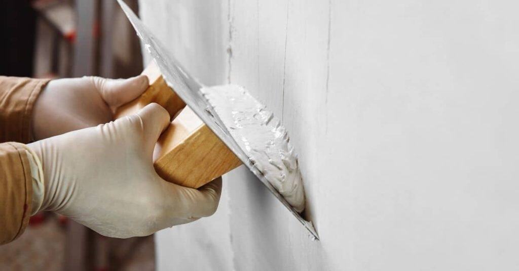Hands wearing gloves applying plaster with a trowel on wall