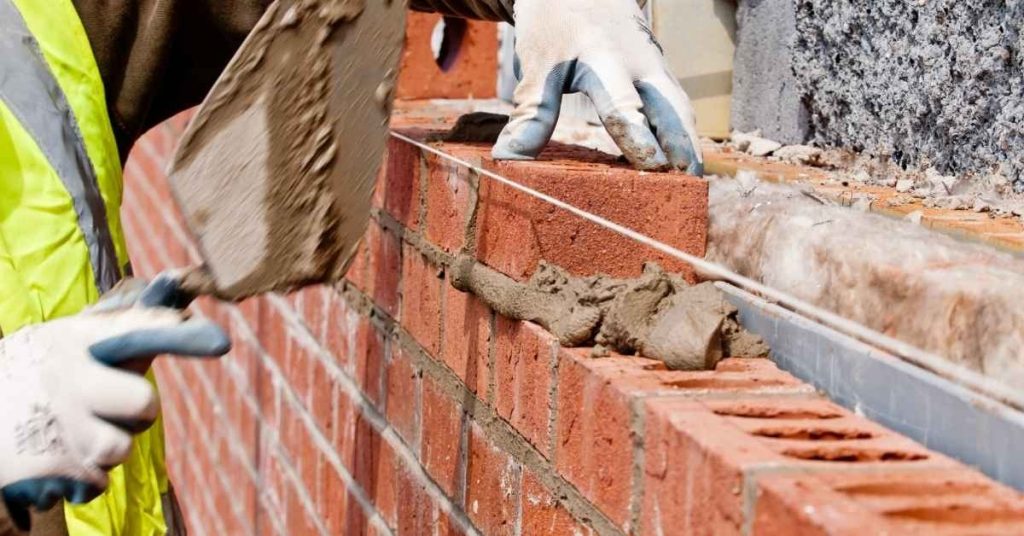 Hands with gloves applying mortar to red brick wall with trowel