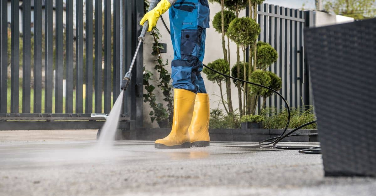 Person in yellow boots pressure washing concrete patio