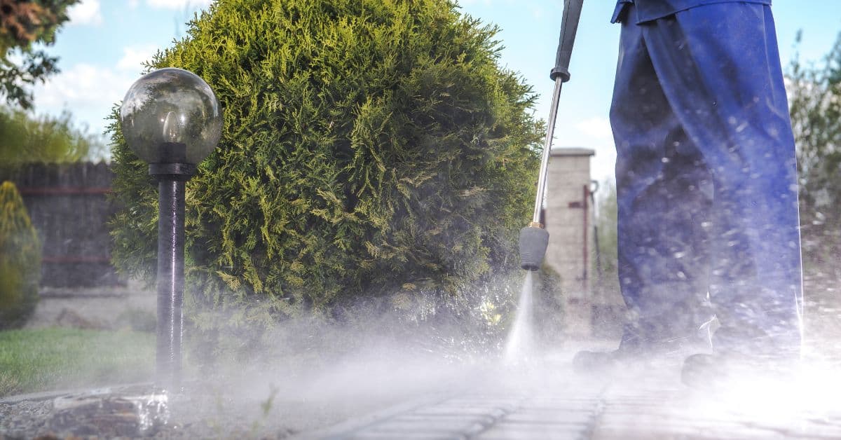 Person using pressure washer on concrete pavers outdoors