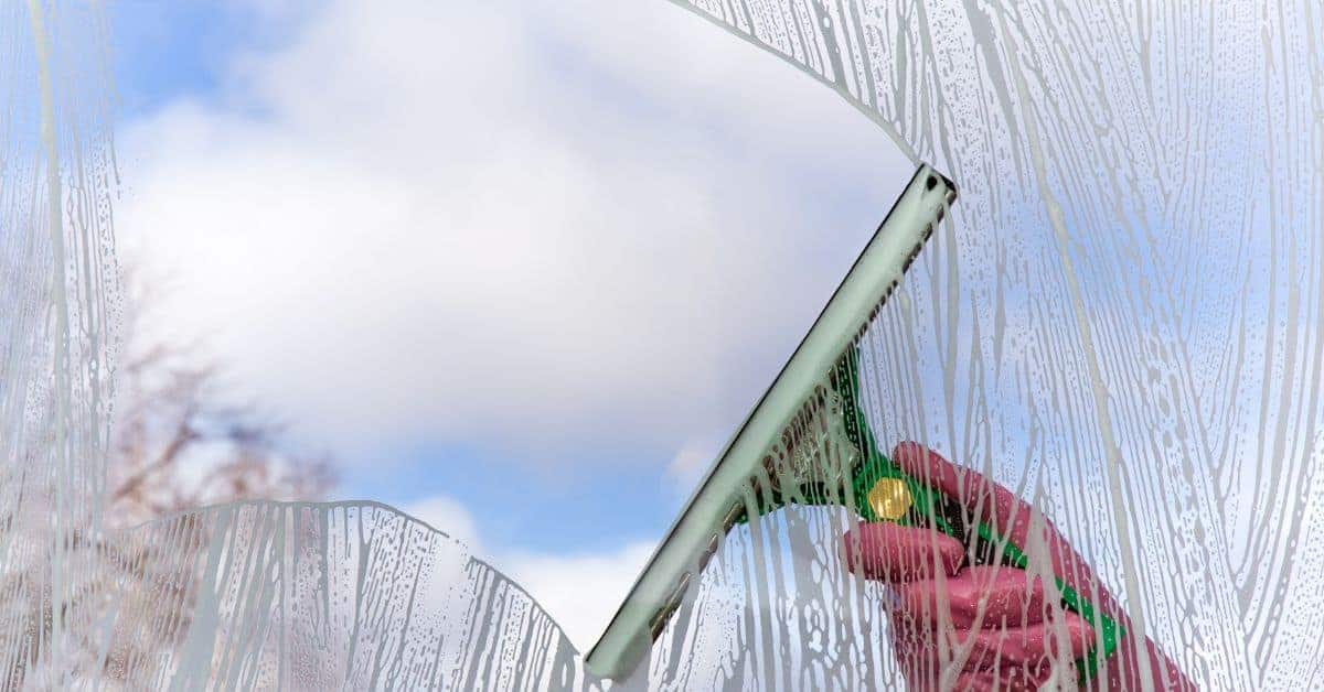Hand using squeegee to clean a glass window outdoors