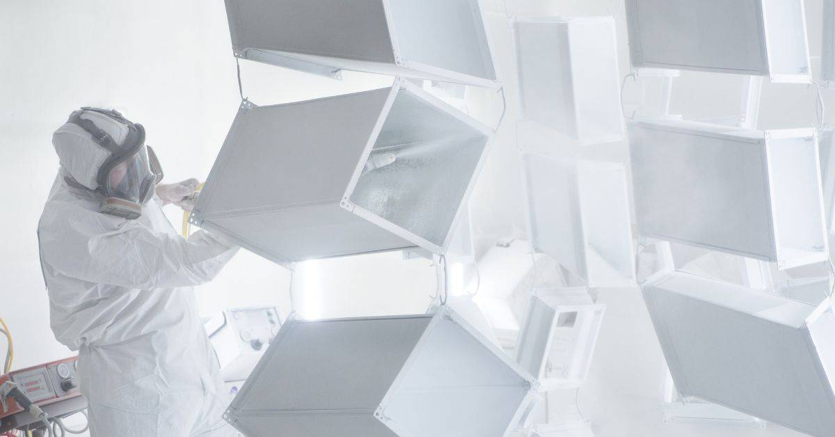 Worker in protective gear inspecting powder-coated metal parts