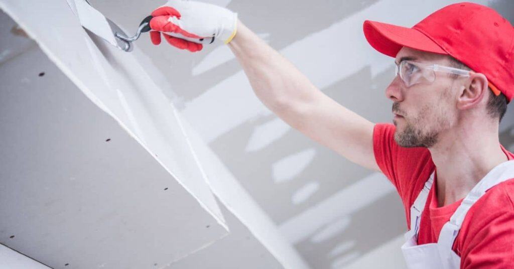 Man applying joint compound to drywall ceiling