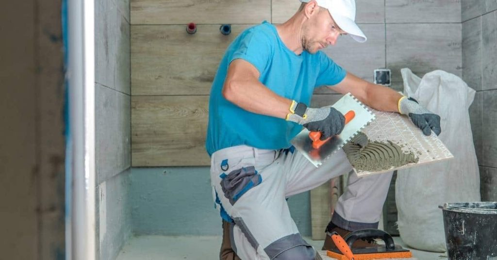 Man applying mortar to the back of a tile with notched trowel
