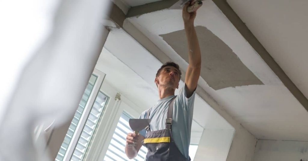 Man applying plaster patch to ceiling near vent