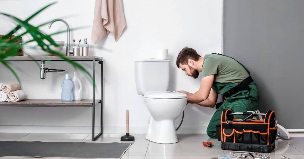 Man fixing toilet bowl with tools nearby in bathroom