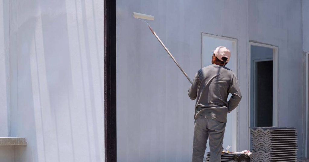 Man painting exterior wall with roller and extension pole