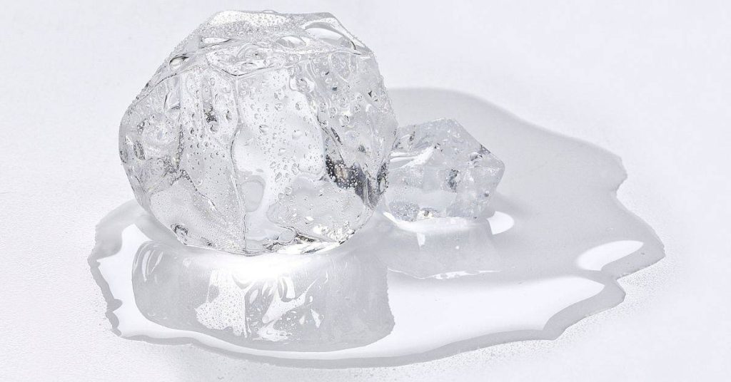 Melting ice cubes with water pool on white surface