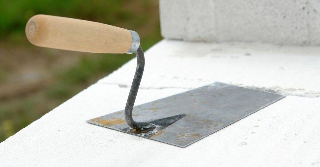 Metal plastering trowel with wooden handle on white plaster surface