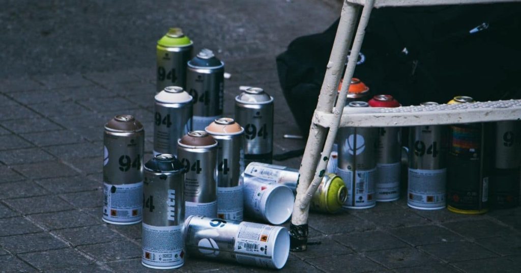 Multiple spray paint cans clustered on pavement near metal frame