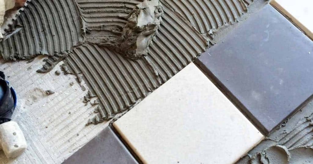 Notched trowel spreading tile adhesive on floor