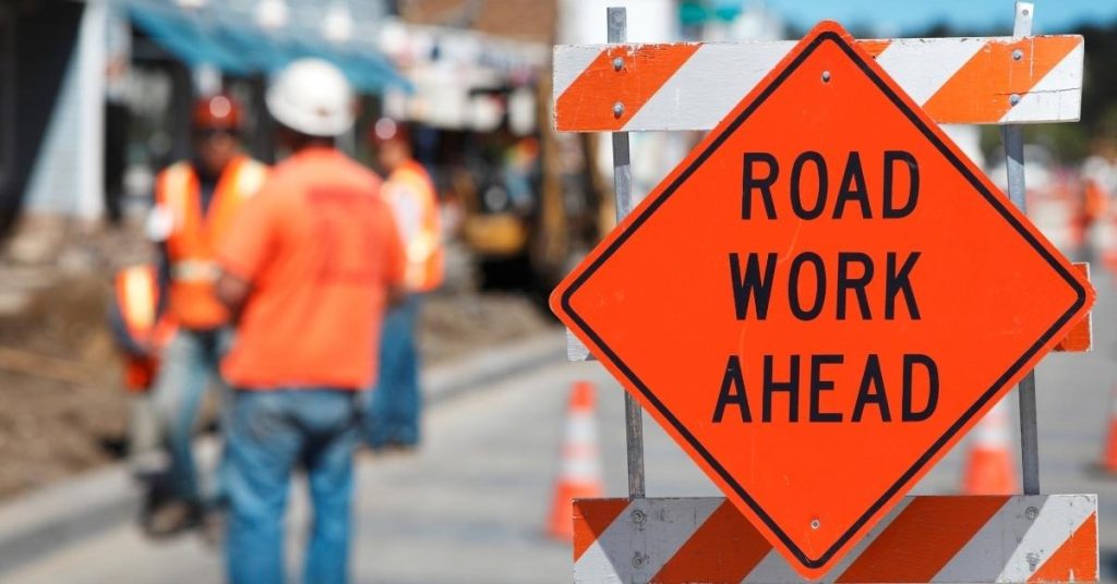 Orange road work ahead sign with workers in safety gear