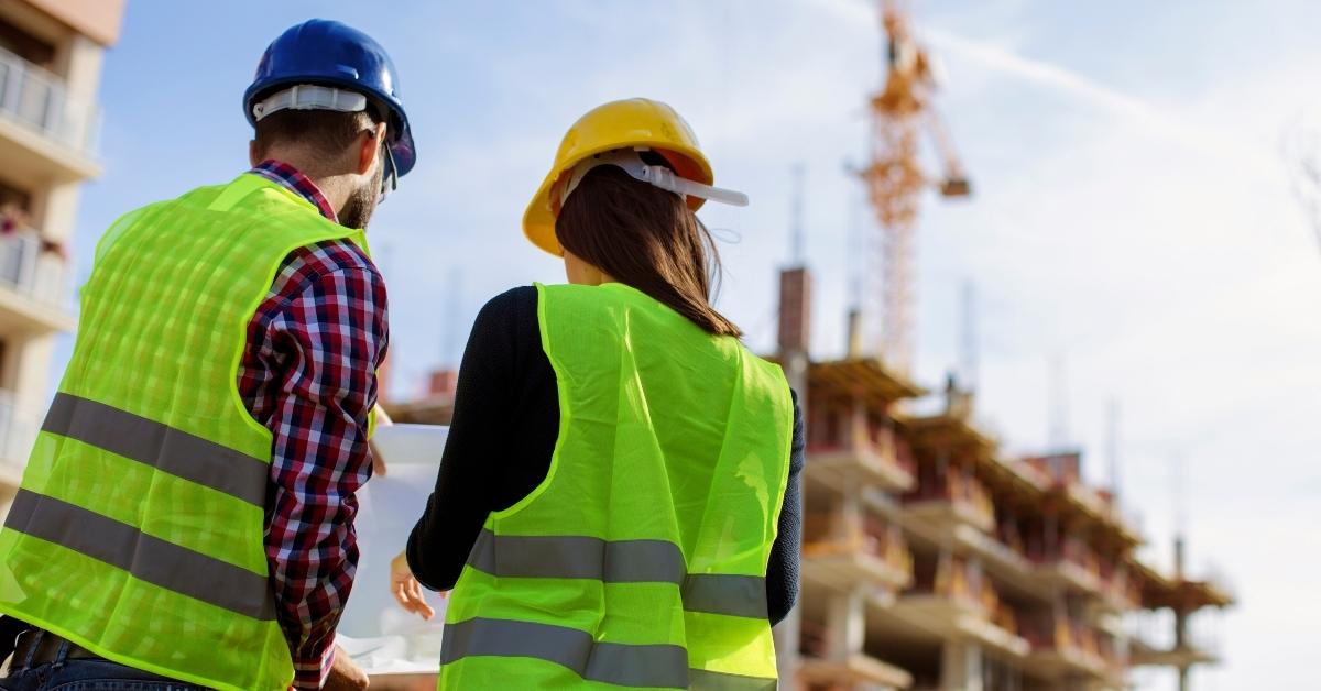 Two construction workers in helmets and safety vests reviewing plans