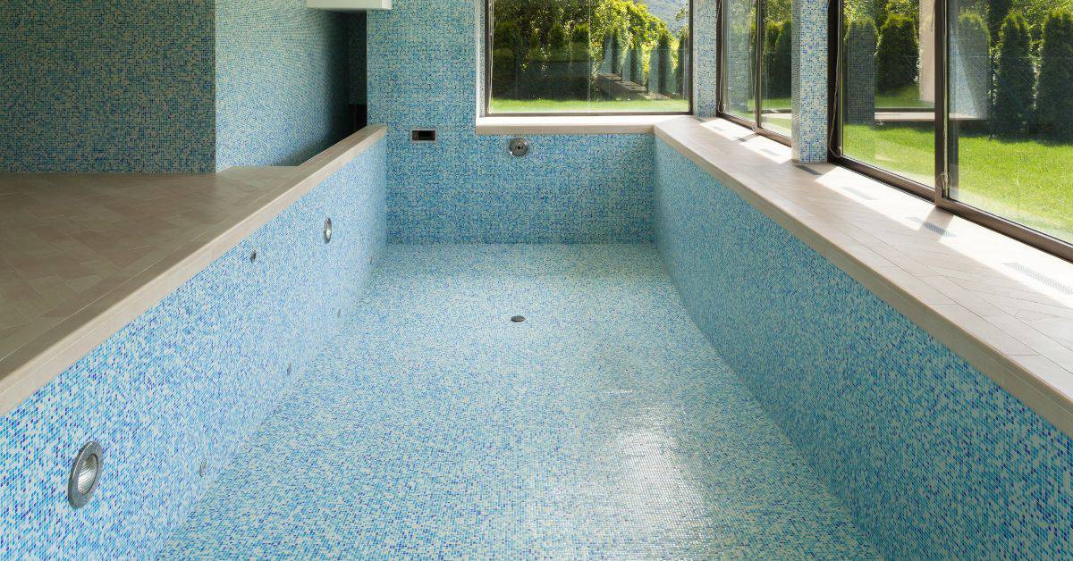 Empty indoor pool with blue mosaic tiles and large windows