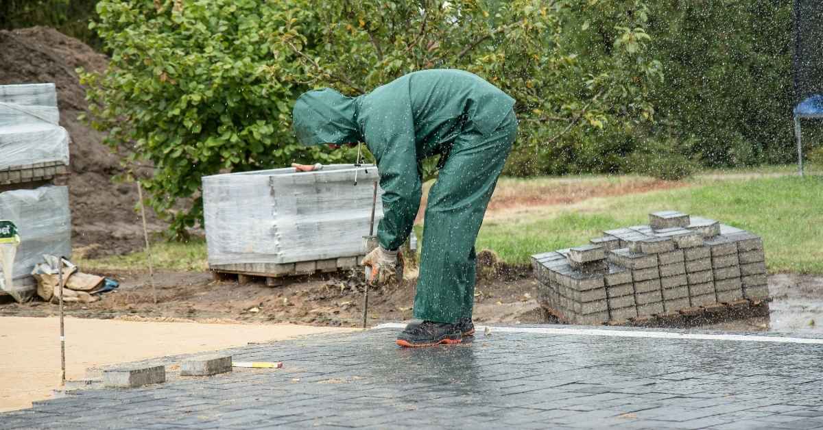 Worker in raincoat installing outdoor pavers in the rain