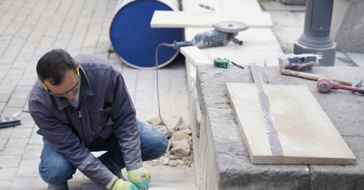worker kneeling installing paving tiles on ground