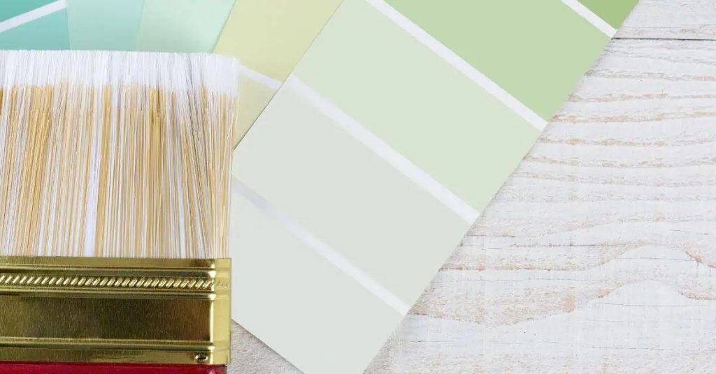 Paint brush and green paint color swatches on wooden surface