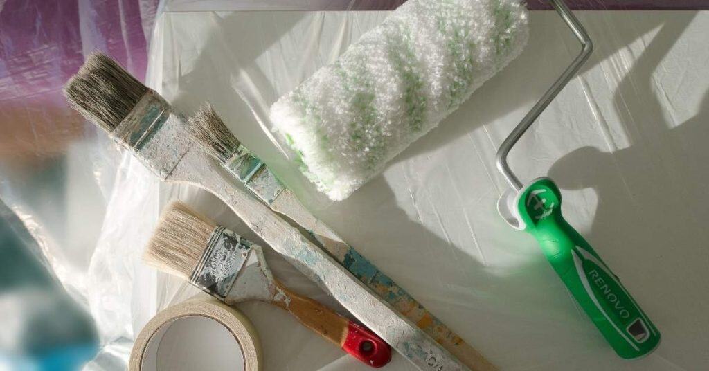 Paint brushes, paint roller, and masking tape on plastic sheet