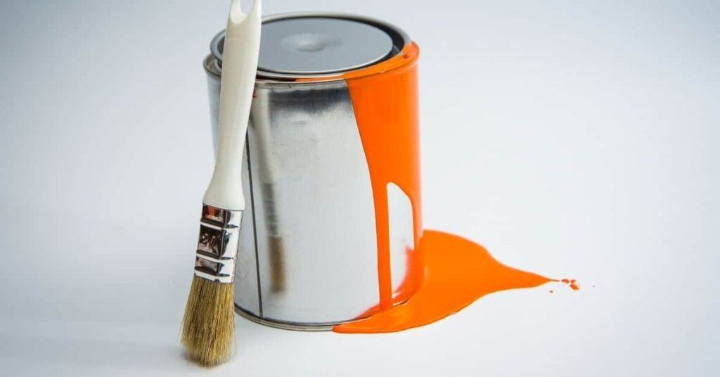 Paint can with orange paint dripping and brush leaning