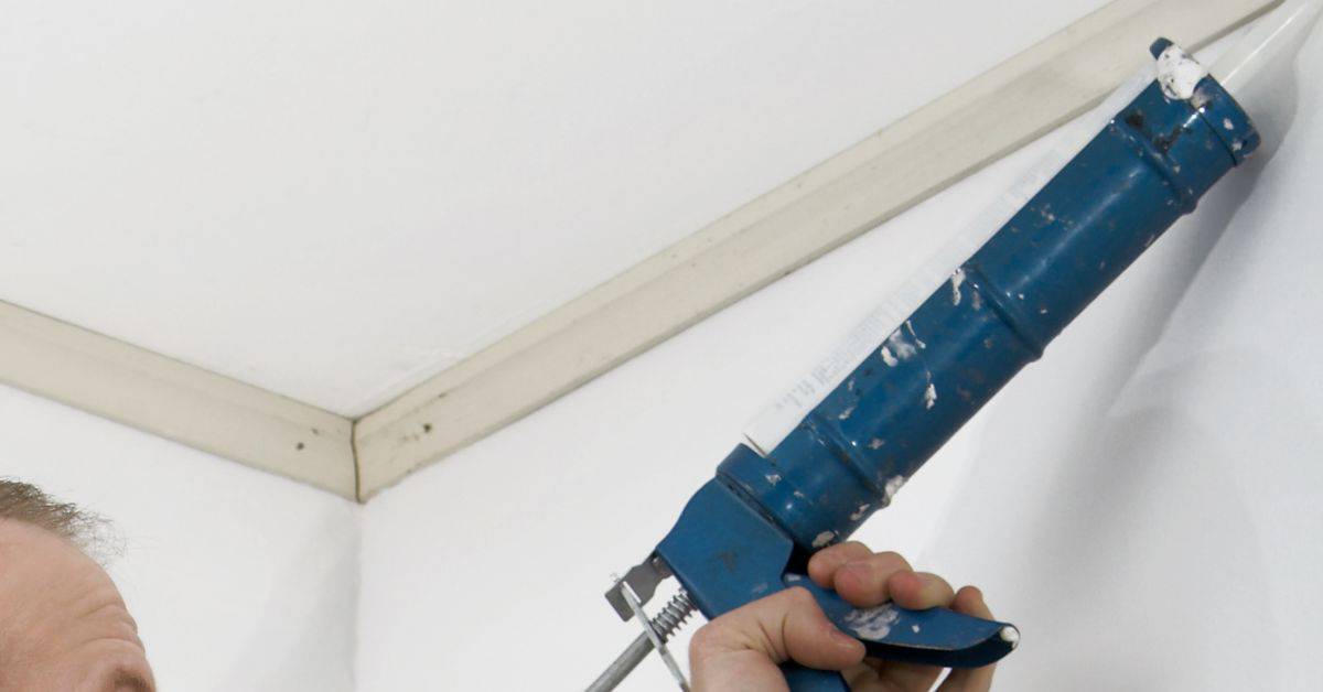 Hand holding blue caulking gun applying sealant in corner