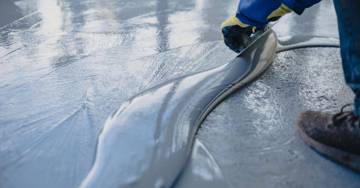 Worker spreading epoxy coating on concrete floor with gloved hand