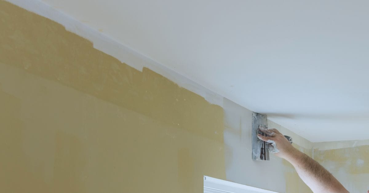 Hand applying spackle to a drywall corner with a metal tool