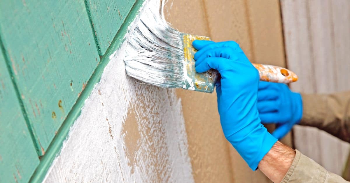 Person wearing blue gloves applying white primer on wood siding