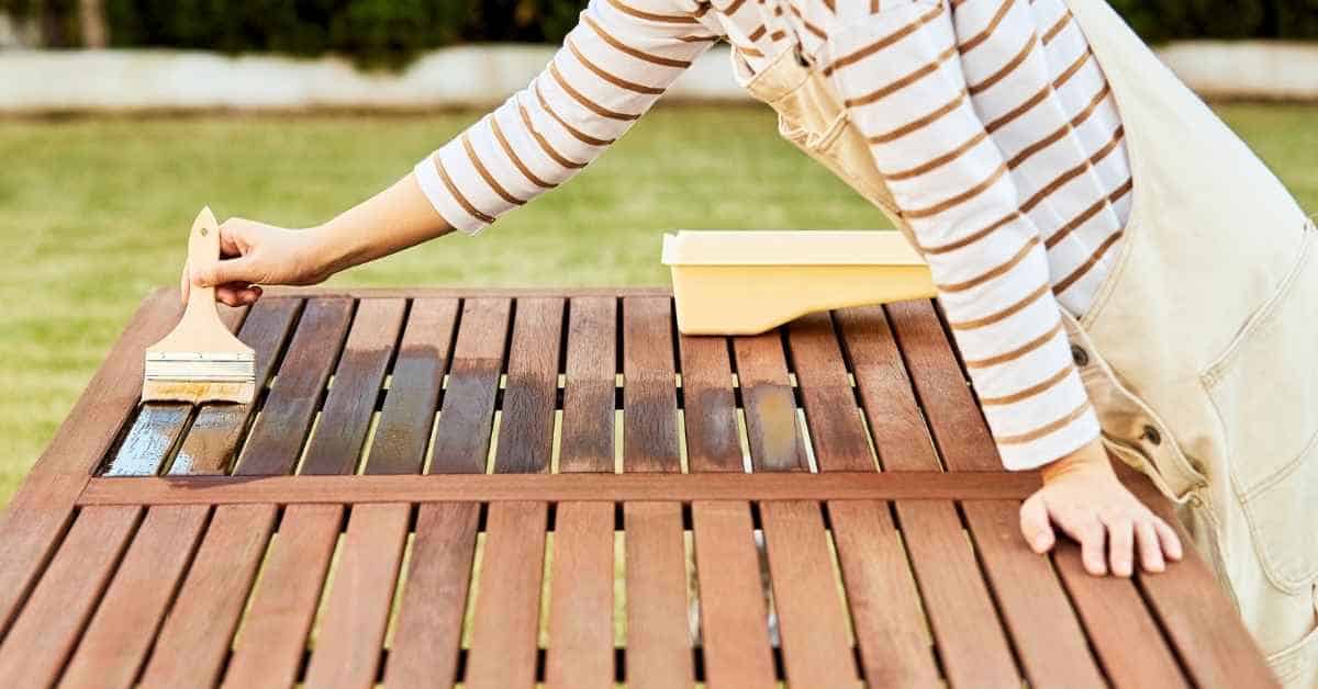 Person applying stain or finish to wooden outdoor furniture
