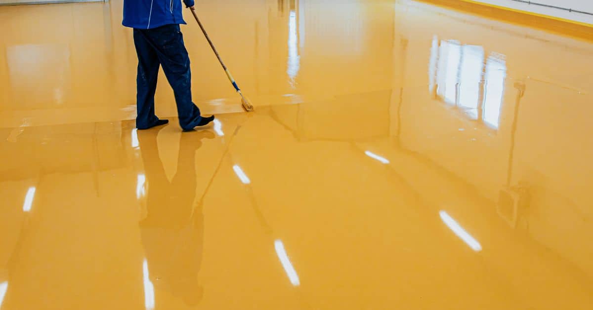 Person applying yellow epoxy coating on garage floor with roller