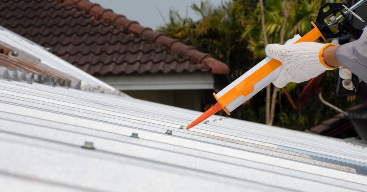 Hand applying sealant to seams of white metal roof panels