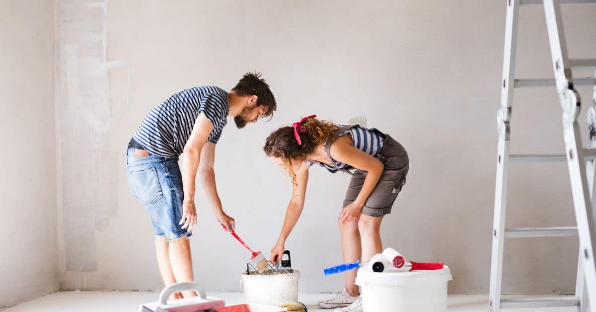 man and woman preparing paint tools in empty room