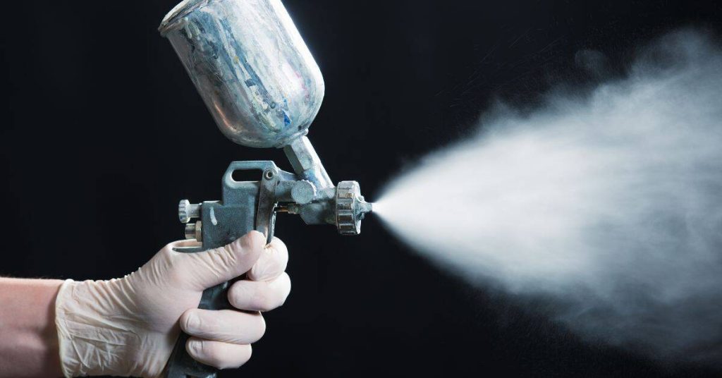 Hand holding spray paint gun emitting fine mist