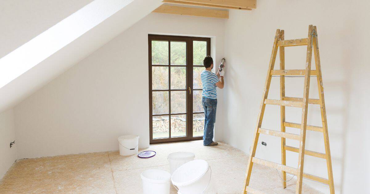 Man using power sander on wall near window in empty room